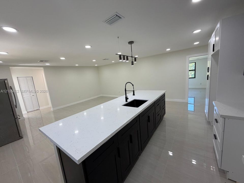 Kitchen island featuring dark cabinetry, quartz countertops, a recessed sink with a high-arch pull-down faucet, and overhead pendant lighting, complemented by polished tile flooring and recessed ceiling lights