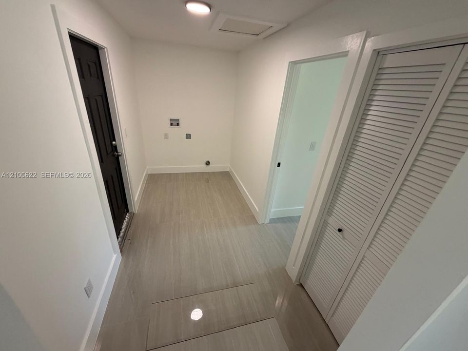 Utility space featuring wood-finish flooring, a dark-toned door with paneled detailing, white louvered-style closet doors, and flush-mount ceiling lighting