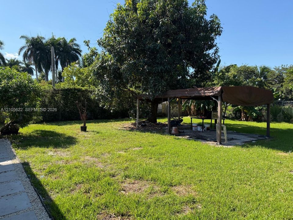 Expansive backyard featuring a sprawling lawn, mature trees, a paved stone walkway, and an open-air metal structure