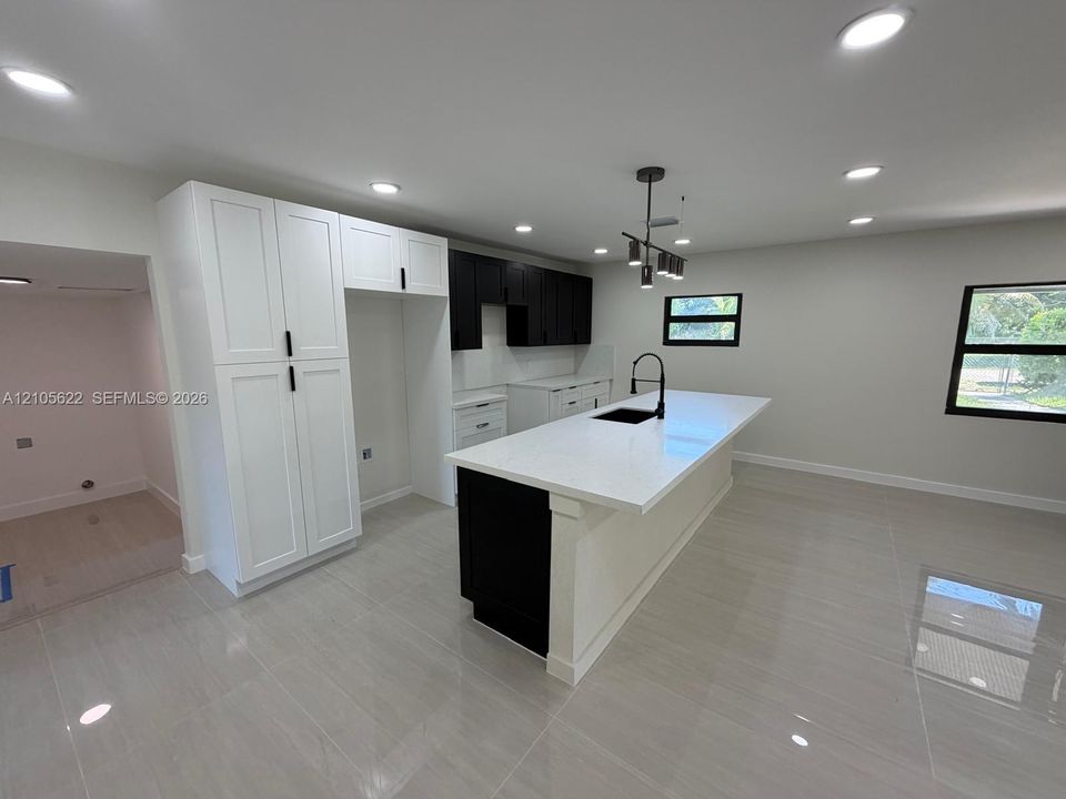 Kitchen featuring high-contrast cabinetry, an expansive center island with a stone countertop, an integrated undermount sink with a matte black faucet, recessed lighting, and large-format tile flooring