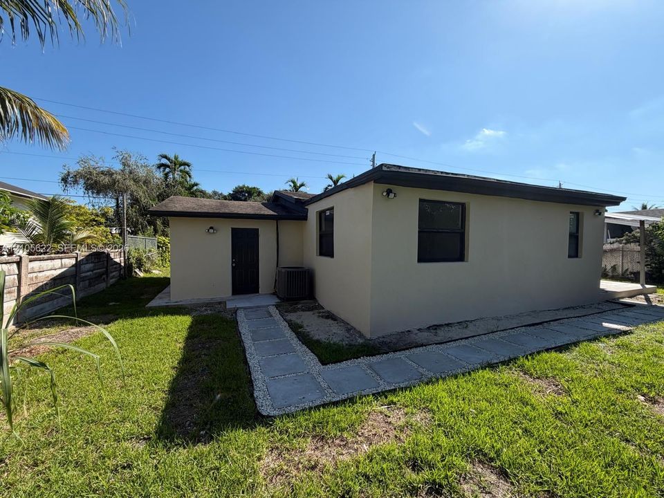 Stucco exterior featuring dark-framed windows, a dedicated entry point, and concrete paver pathway set within a grass lawn