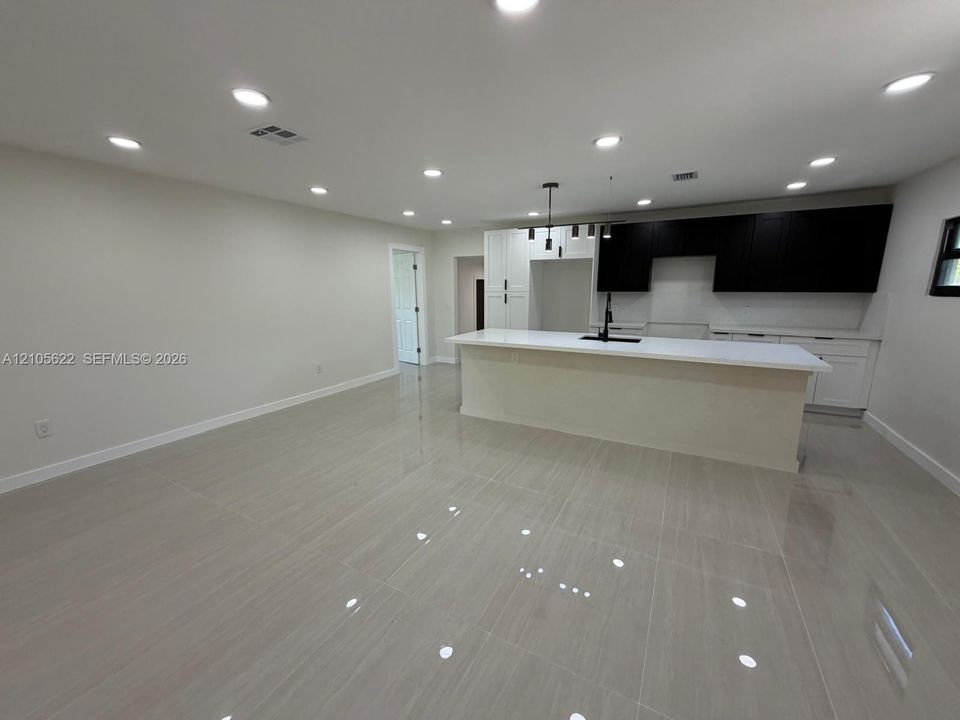 Open-concept kitchen featuring two-tone cabinetry, a central island with a stone-finish countertop, recessed ceiling lighting, and large-format tile flooring