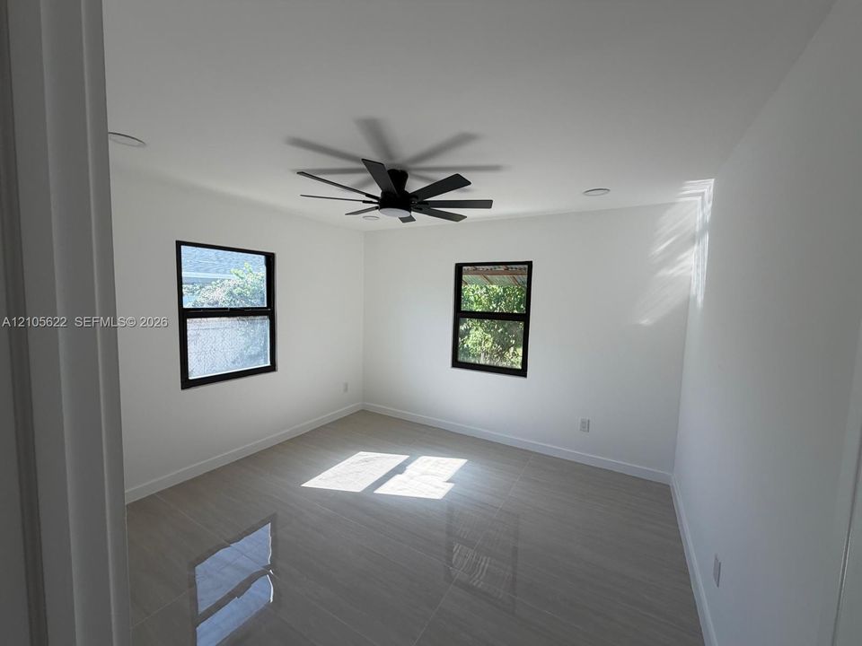 Interior space featuring neutral wall paint, polished tile flooring, recessed lighting, and a modern black ceiling fan with dual-pane windows framed in black