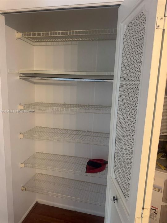 Storage closet featuring five tiered wire shelves, a hanging rod, and a hinged door with a decorative perforated panel