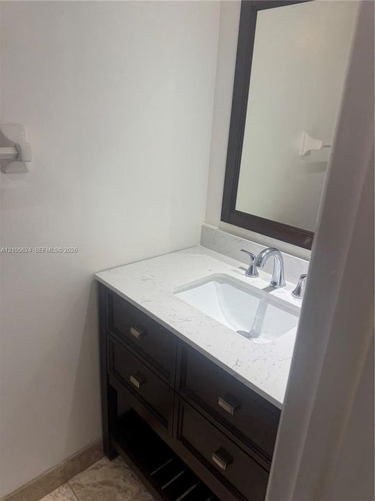 Dark wood vanity featuring four storage drawers, an open bottom shelf, a light-toned stone-look countertop with an integrated basin, and a chrome widespread faucet