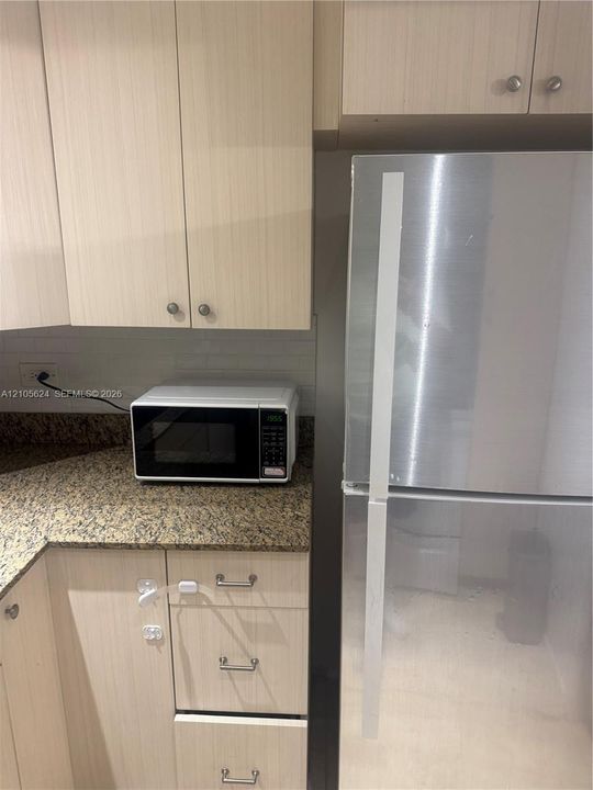 Light-toned cabinetry with metal hardware, stone-finish countertops, subway tile backsplash, and a stainless steel refrigerator