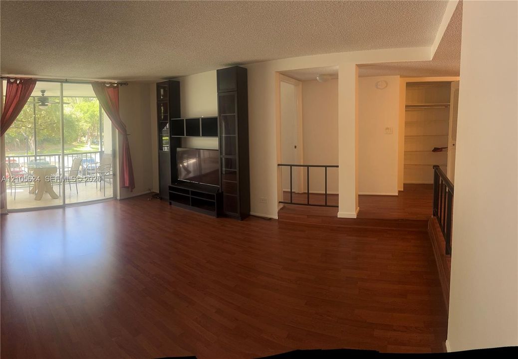 Wood-finish flooring throughout, built-in black shelving unit, sliding glass doors to a covered balcony, and elevated platform area with metal handrailing