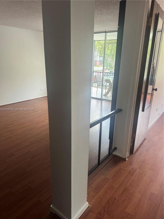 Interior space featuring wood-finish flooring, a structural support column, a black metal railing, and sliding glass doors with screen enclosure