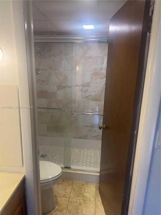 Bathroom featuring a walk-in shower with glass sliding doors, floor-to-ceiling neutral-toned wall tile, and large-format tile flooring