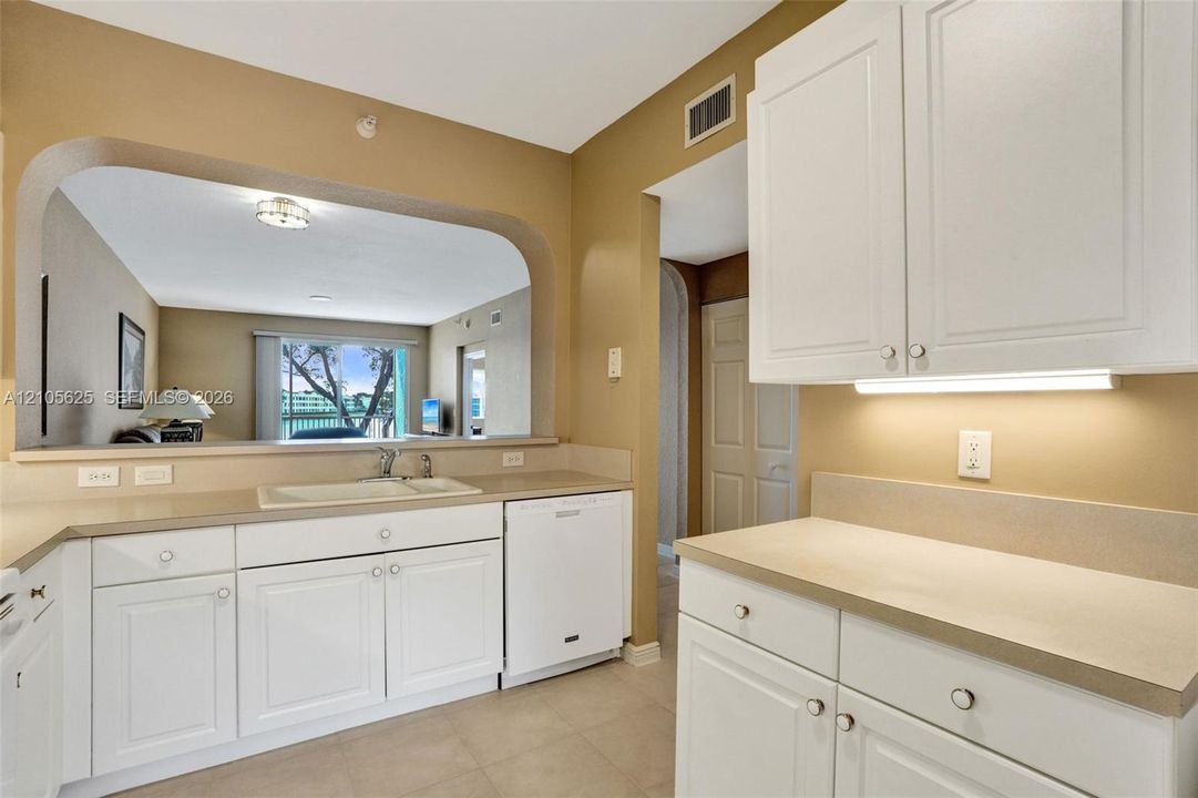 Kitchen featuring white cabinetry, solid surface countertops, integrated dishwasher, and a pass-through opening
