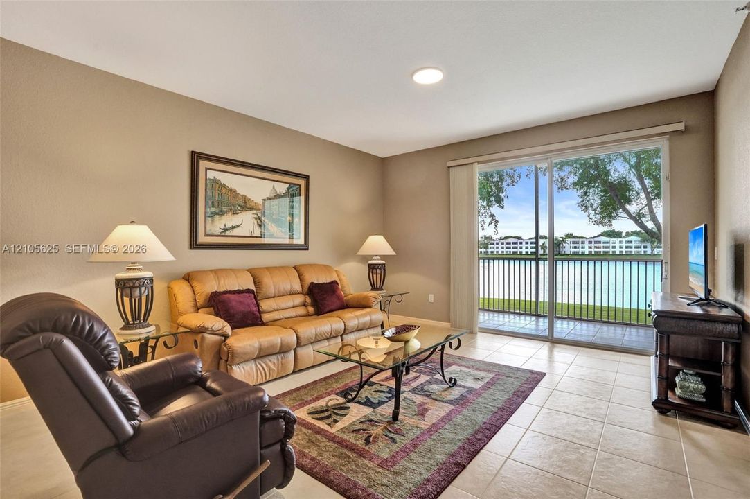 Neutral-toned interior featuring large-format ceramic tile flooring, recessed lighting, and a sliding glass door providing water access to a private balcony with metal railings