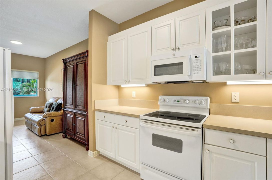 Kitchen featuring white shaker-style cabinetry, solid-surface countertops, under-cabinet lighting, a built-in microwave, and glass-paneled upper cabinet doors