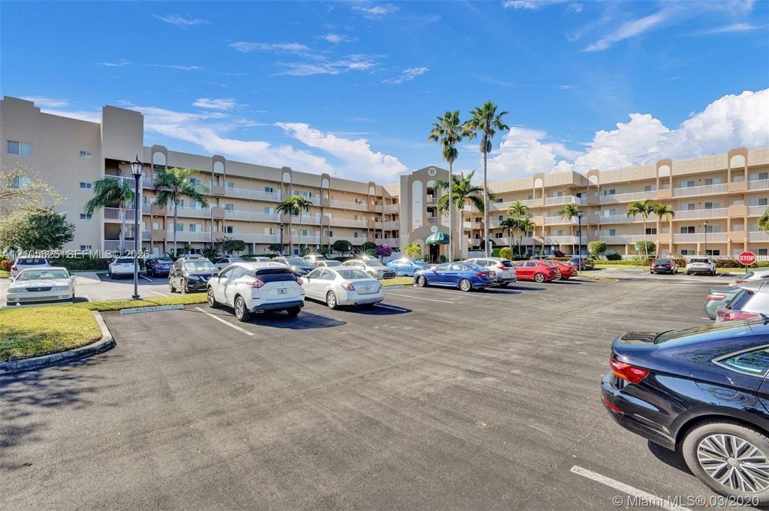Multi-story residential complex featuring stucco exterior walls, private balconies, paved surface parking, and mature palm trees