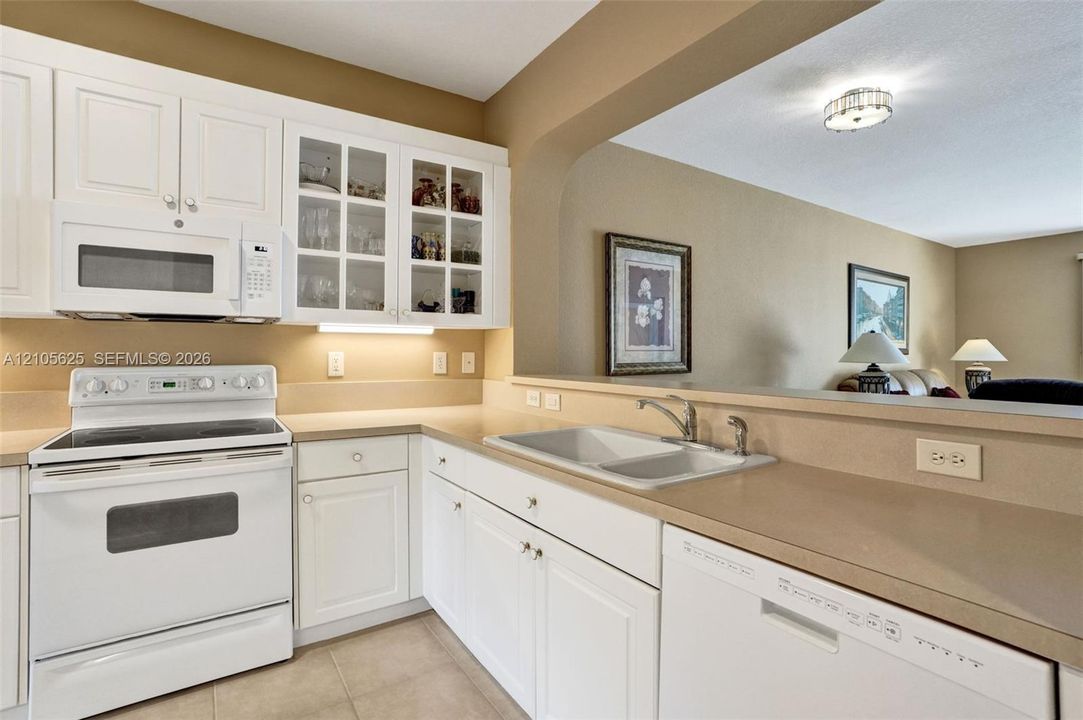 Kitchen featuring white shaker-style cabinetry, glass-front upper cabinet doors, solid-surface countertops, dual-basin sink with metallic faucet, and built-in appliances