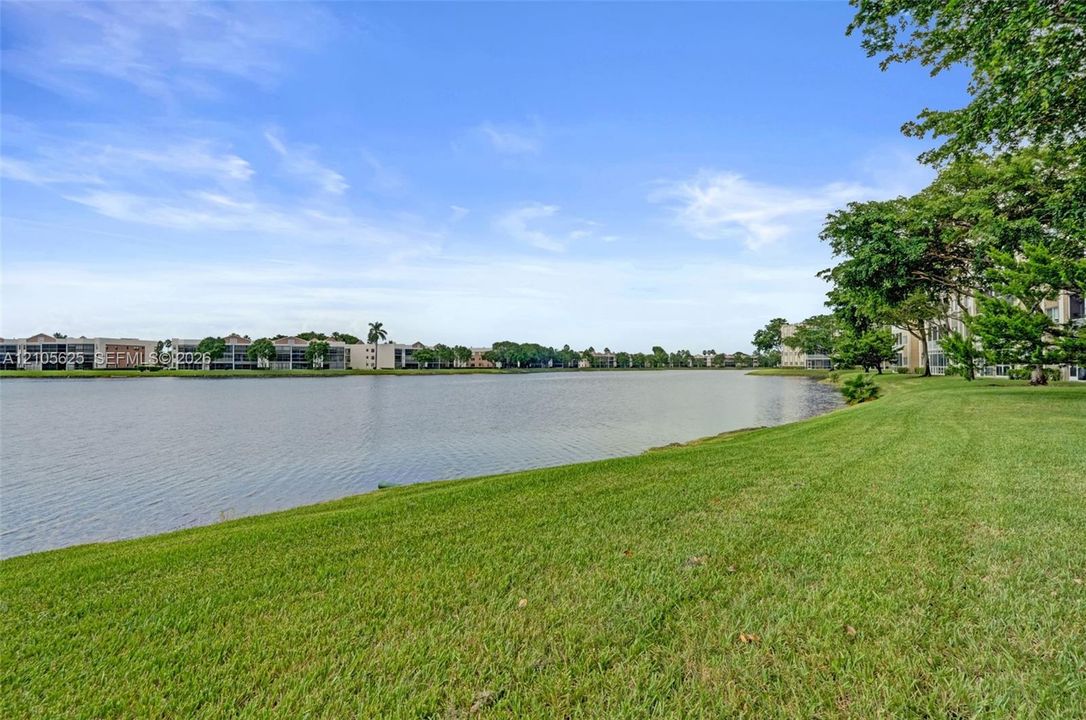 Waterfront grounds featuring a maintained lawn, mature trees, and a lake
