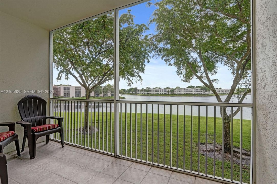 Screen-enclosed patio featuring a tiled floor and metal railing, overlooking a lake and mature trees