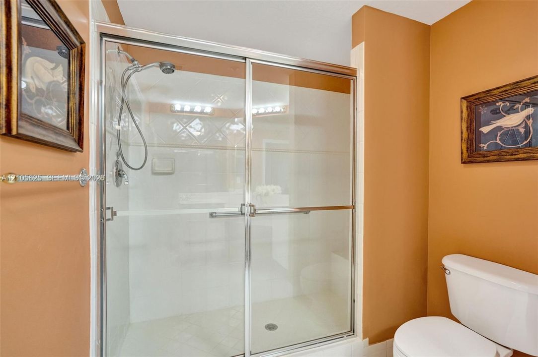 Shower stall featuring sliding glass doors, polished chrome hardware, an adjustable handheld showerhead, and a built-in soap dish