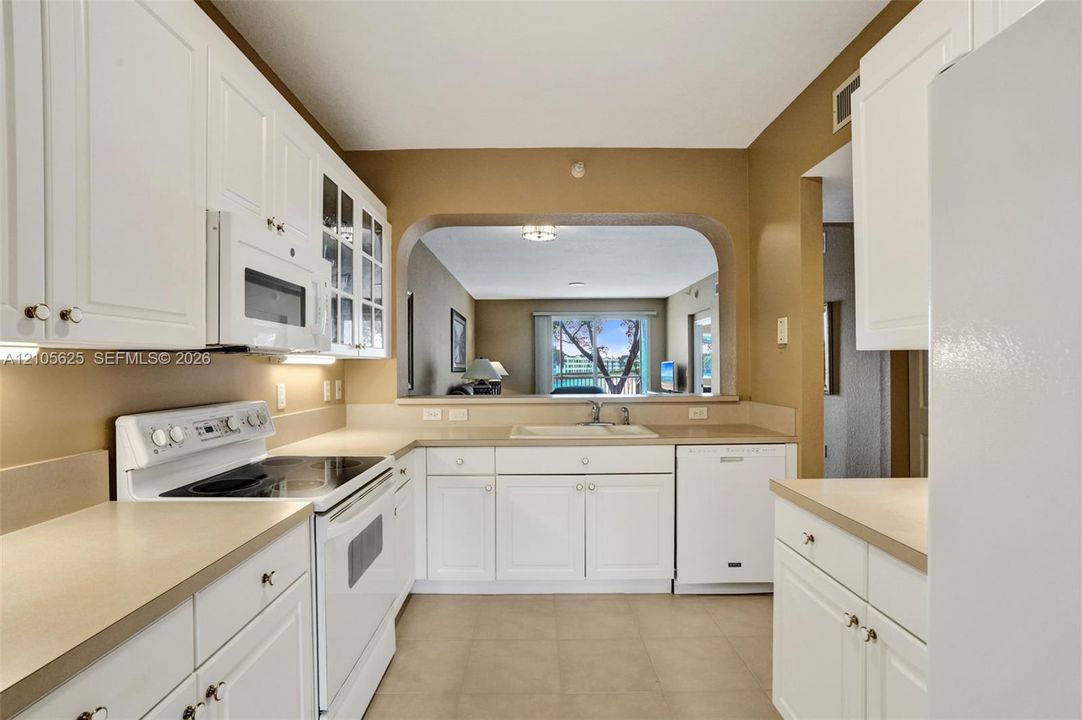 Kitchen featuring white cabinetry with glass-panel upper doors, solid-surface countertops, tile flooring, and a passthrough opening