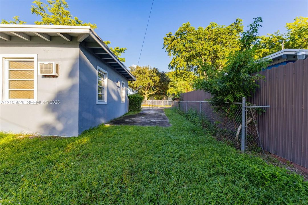 Exterior featuring smooth-finish stucco siding, multi-pane windows, a concrete ground-level surface, chain-link perimeter fencing, and corrugated metal screening