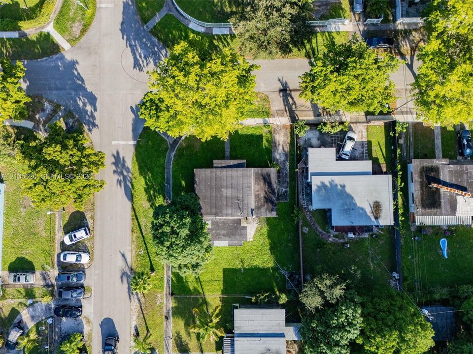 Aerial view of a corner lot property featuring expansive lawn space, mature landscaping, and an asphalt shingle roof