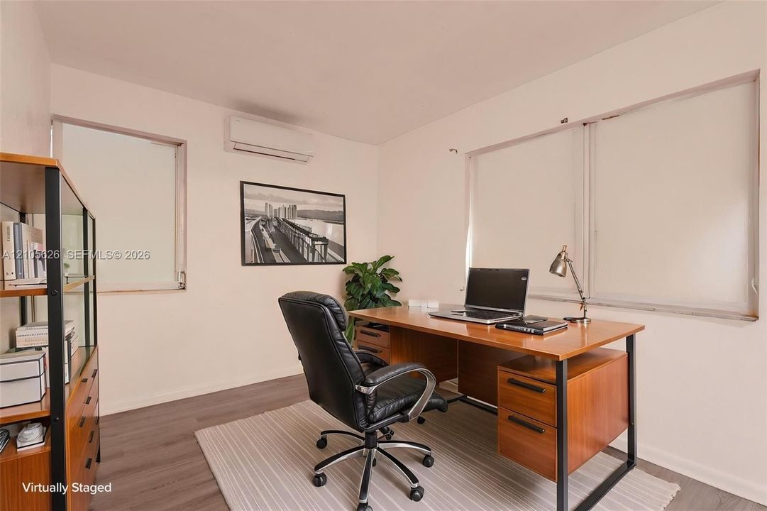 Room featuring wood-finish flooring, three windows with neutral window treatments, and a wall-mounted mini-split HVAC unit