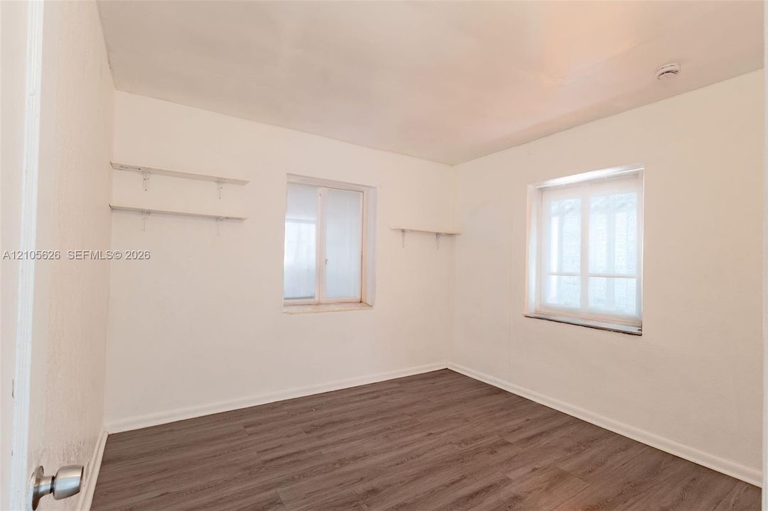 Neutral interior space featuring wood-finish flooring, white walls, dual windows with sills, and built-in wall-mounted shelving