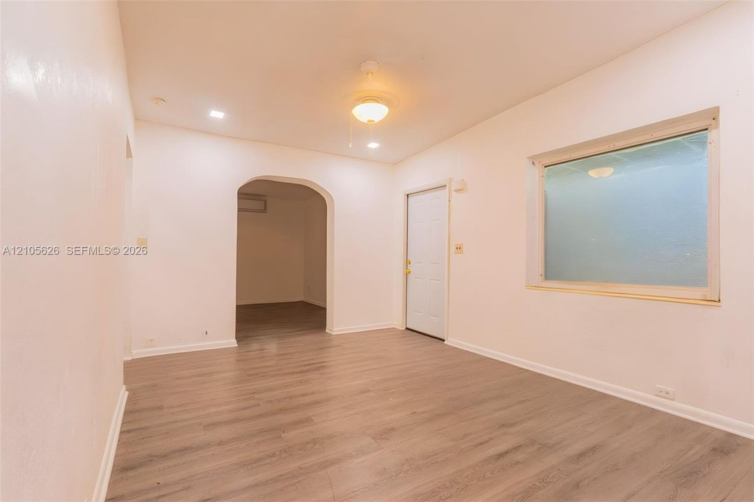 Interior space featuring wood-finish flooring, a recessed arched entryway, a single-panel door, a flush-mount ceiling light fixture, and a large rectangular window