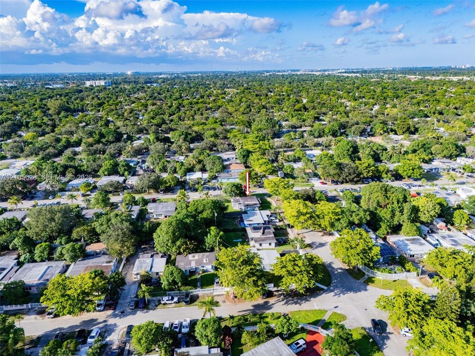 Aerial perspective featuring a detached residential structure with a flat roofline situated on a corner lot with mature canopy trees and expansive landscaping