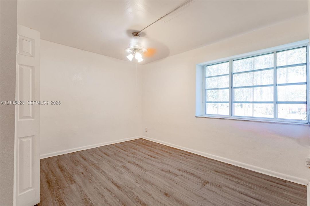 Room featuring wood-finish flooring, a multi-pane window, and a central ceiling fan with an integrated light fixture