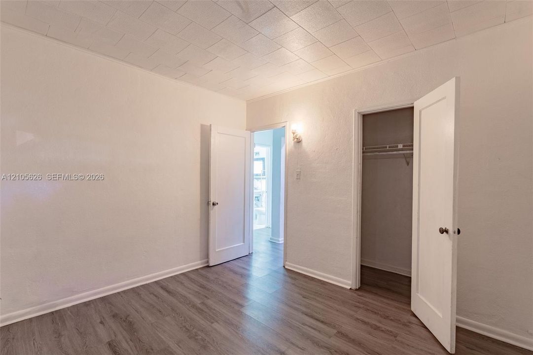 Room featuring wood-finish flooring, textured ceiling, white walls, built-in closet with shelving, and two interior doors