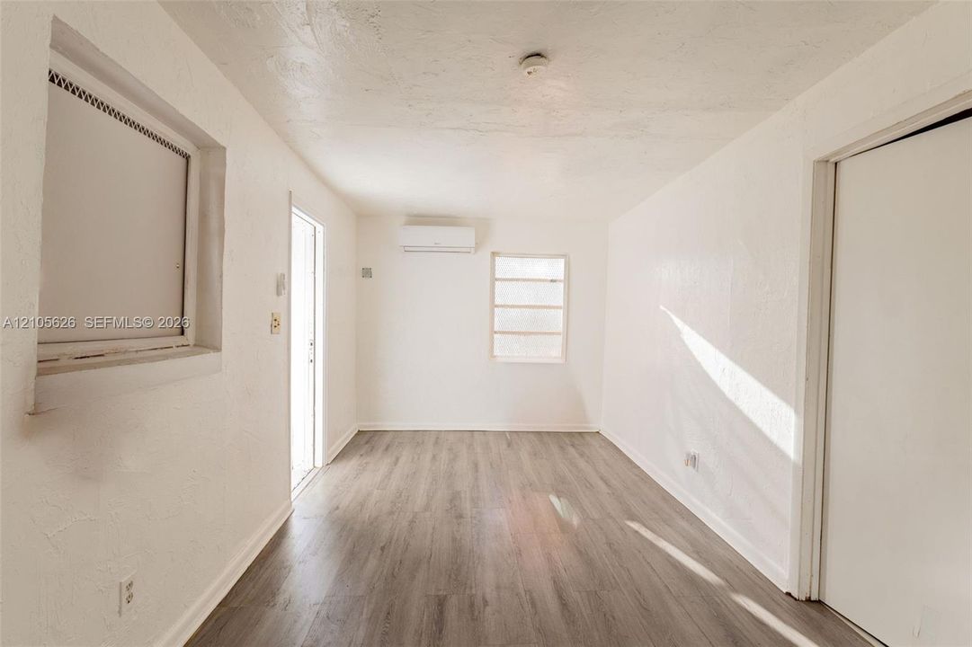 Interior space featuring wood-finish flooring, white wall textures, a wall-mounted ductless climate control unit, and glass-pane windows