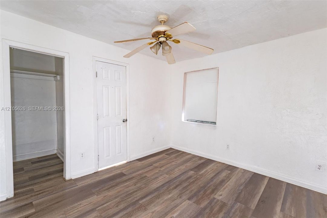 Room featuring wood-finish flooring, a multi-blade ceiling fan with integrated light fixture, a recessed closet space, and a single-panel interior door