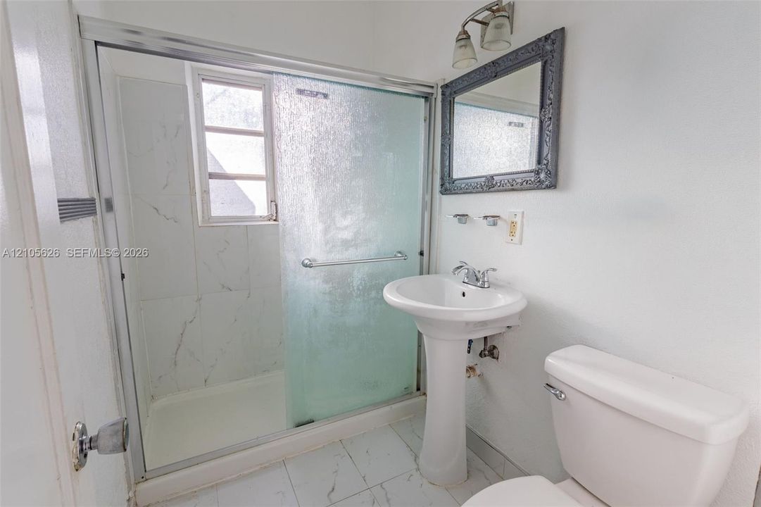 Bathroom featuring a shower stall with a sliding glass door and stone-patterned tile surround, a pedestal sink with a dual-handle faucet, and ceramic tile flooring