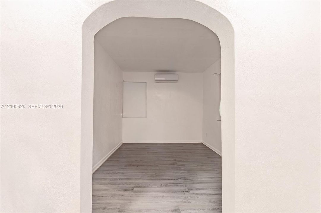 Arched entryway opening to a room with wood-finish flooring and a wall-mounted ductless mini-split system