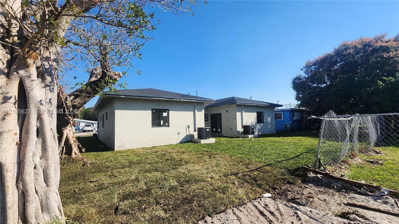 Stucco exterior featuring a hipped roofline, integrated HVAC units, and mature trees on a level lot