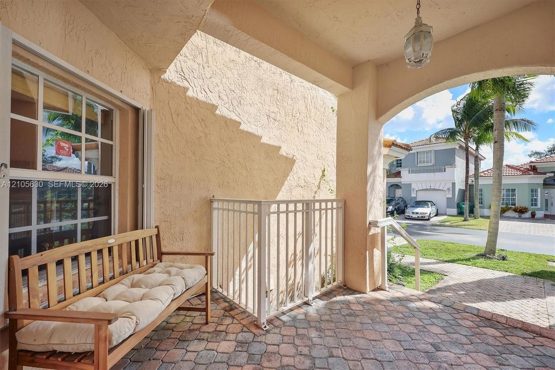 Covered entryway featuring textured stucco walls, paver flooring, a white metal railing, and a hanging pendant light