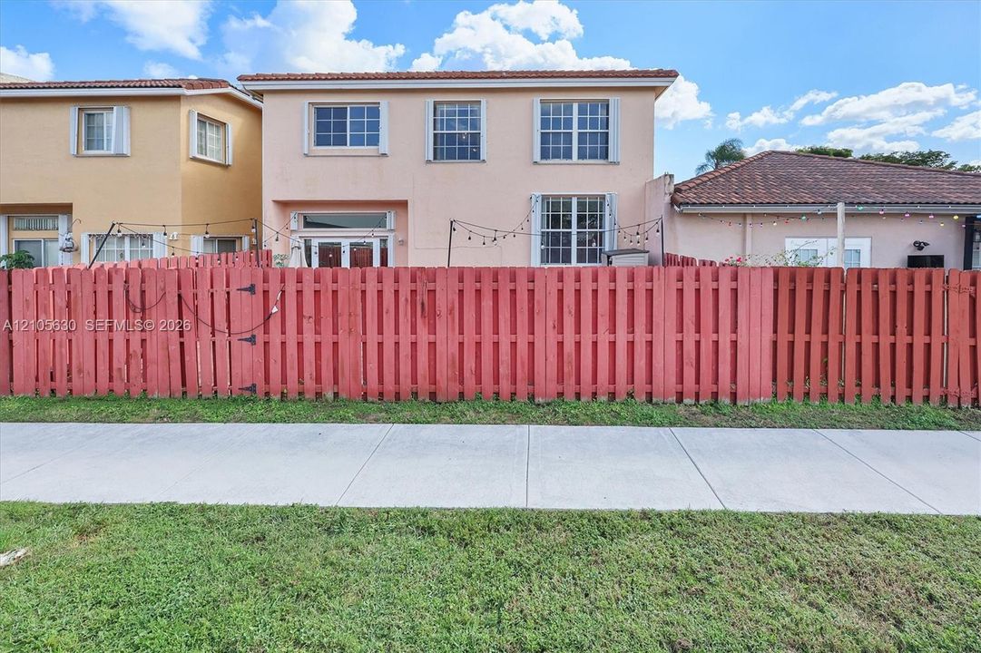 Two-story stucco exterior featuring a red-toned privacy fence, multi-pane windows, and a tiled roofline