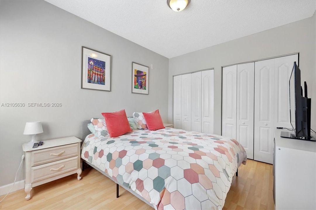 Room featuring wood-finish flooring, neutral wall paint, dual white bi-fold closets, and a central ceiling-mounted light fixture