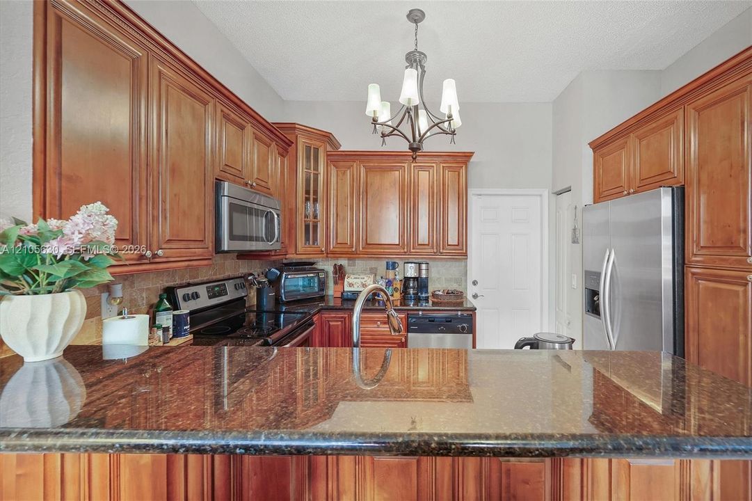 Kitchen featuring wood cabinetry, stone countertops, stainless steel appliances, a multi-light chandelier, and a peninsula-style counter