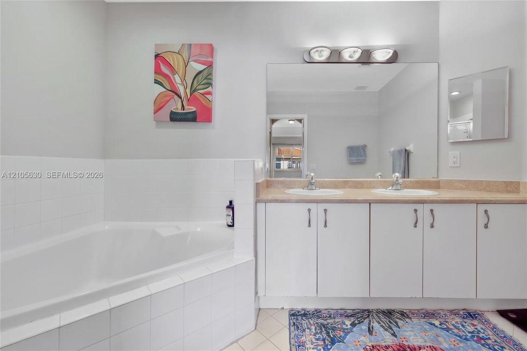 Bathroom featuring a corner soaking tub with white tile surround, dual-sink vanity with light-tone countertop, and three-light overhead vanity fixture