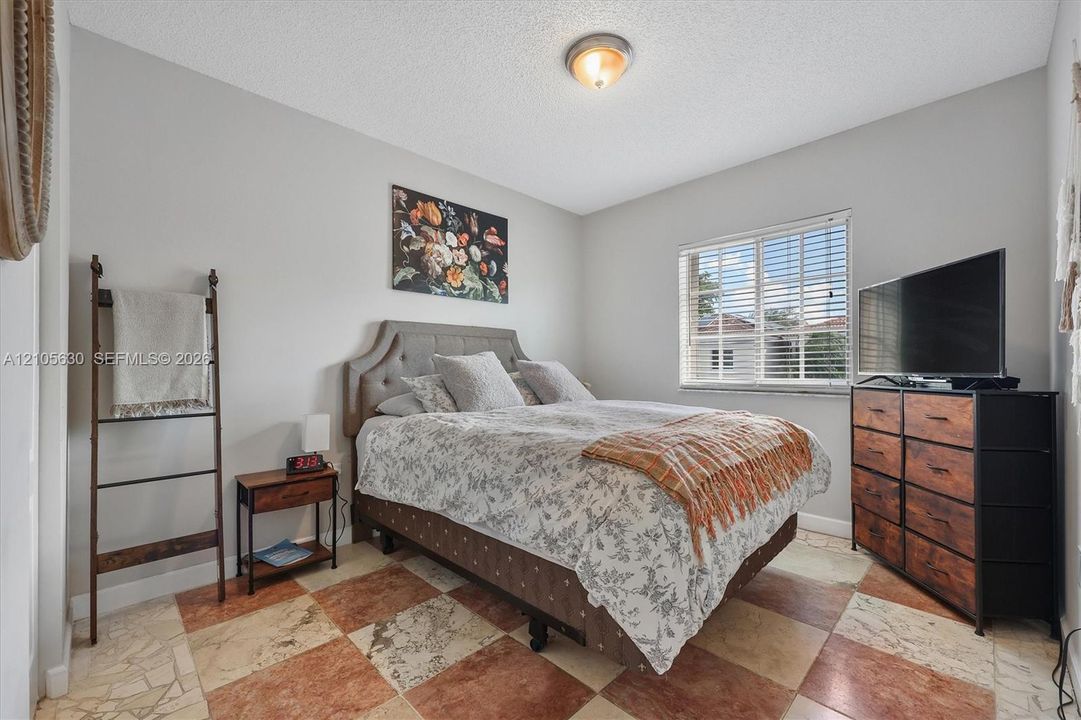 Neutral wall tones, horizontal window blinds, and large-format checkered stone tile flooring