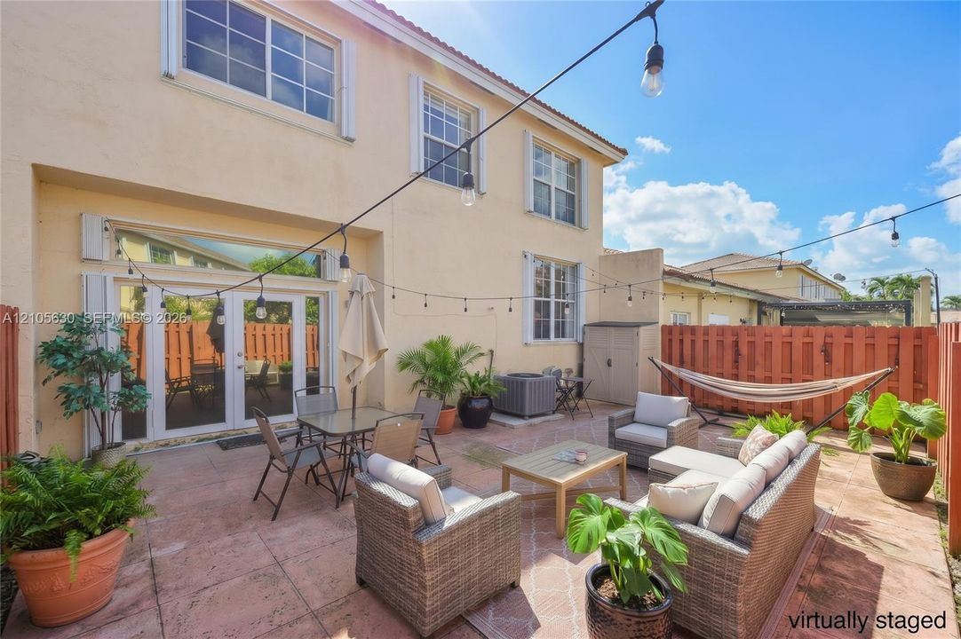 Paved patio featuring double French doors, perimeter wood privacy fencing, and string lighting