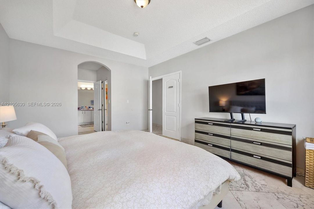 Tray ceiling, arched doorway, and stone-finish tile flooring