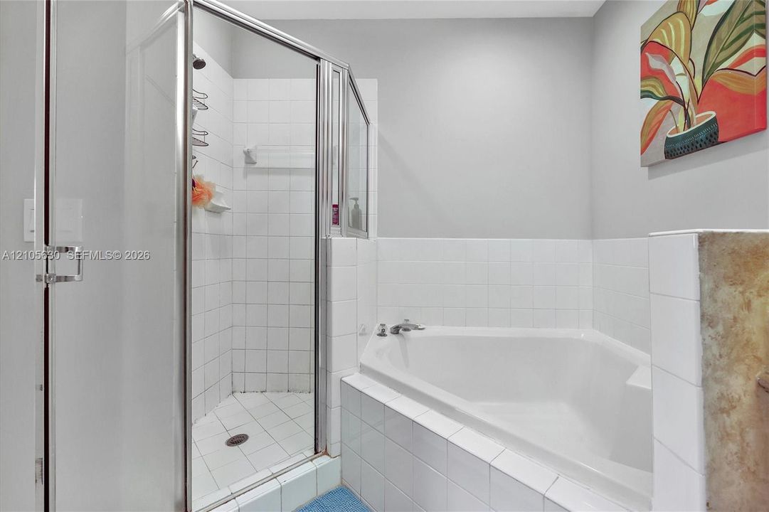 Corner soaking tub and separate shower enclosure featuring white ceramic tile surround and chrome fixtures