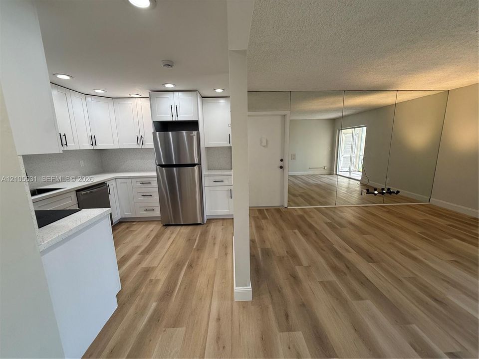 Kitchen featuring white shaker-style cabinetry, stainless steel appliances, and solid-surface countertops, complemented by wood-finish flooring and full-height wall mirrors