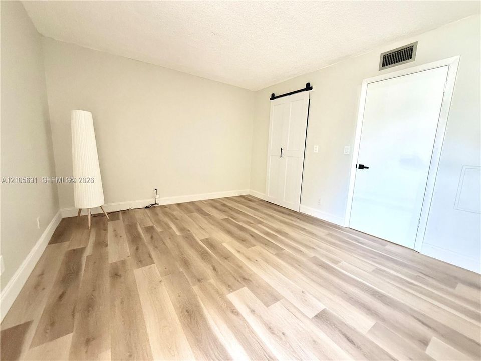 Room featuring wood-finish flooring, white double sliding barn door with matte black hardware, and a solid-panel door with a matte black lever handle
