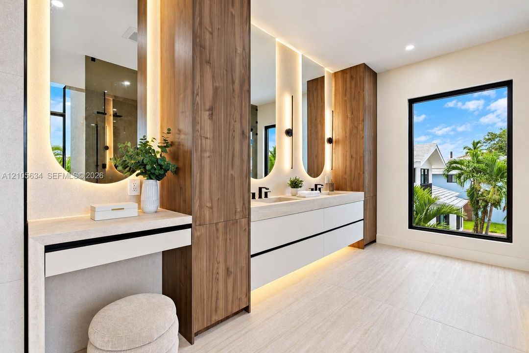 Floating double vanity with integrated wood-finish cabinetry, arched mirrors with perimeter lighting, stone-top surfaces, and matte black fixtures