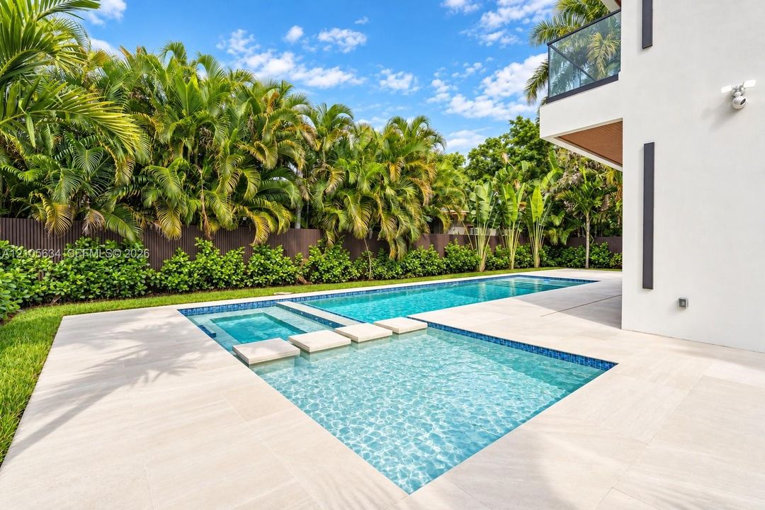 In-ground swimming pool with an integrated spa, featuring stone-style paver decking, decorative concrete stepping stones, and surrounding lush landscaping