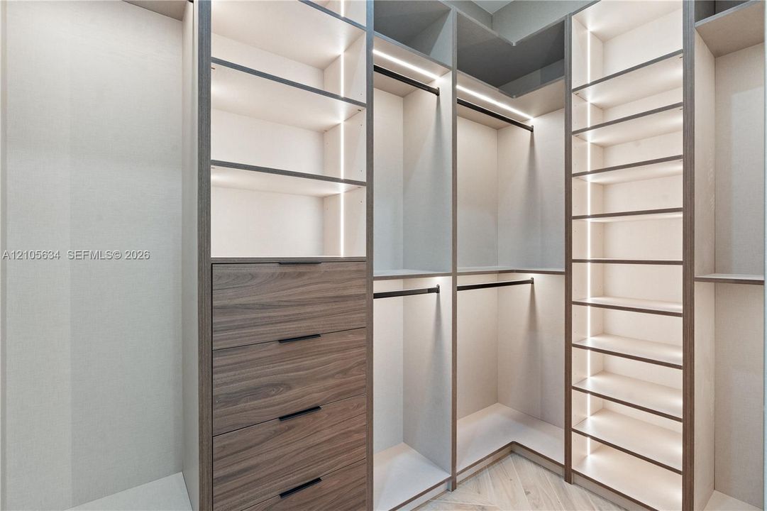 Custom floor-to-ceiling built-in cabinetry featuring wood-finish drawer fronts, integrated linear vertical lighting, adjustable open shelving, and matte black hardware