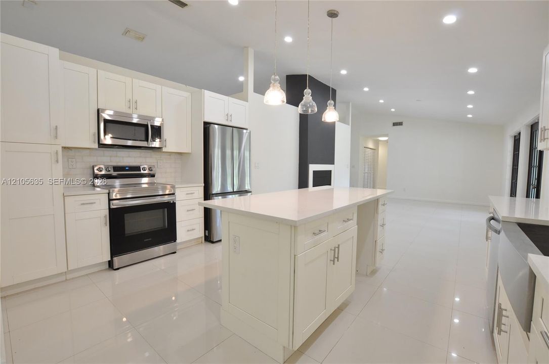 Kitchen featuring white shaker-style cabinetry, quartz countertops, stainless steel appliances, a central island, and recessed lighting